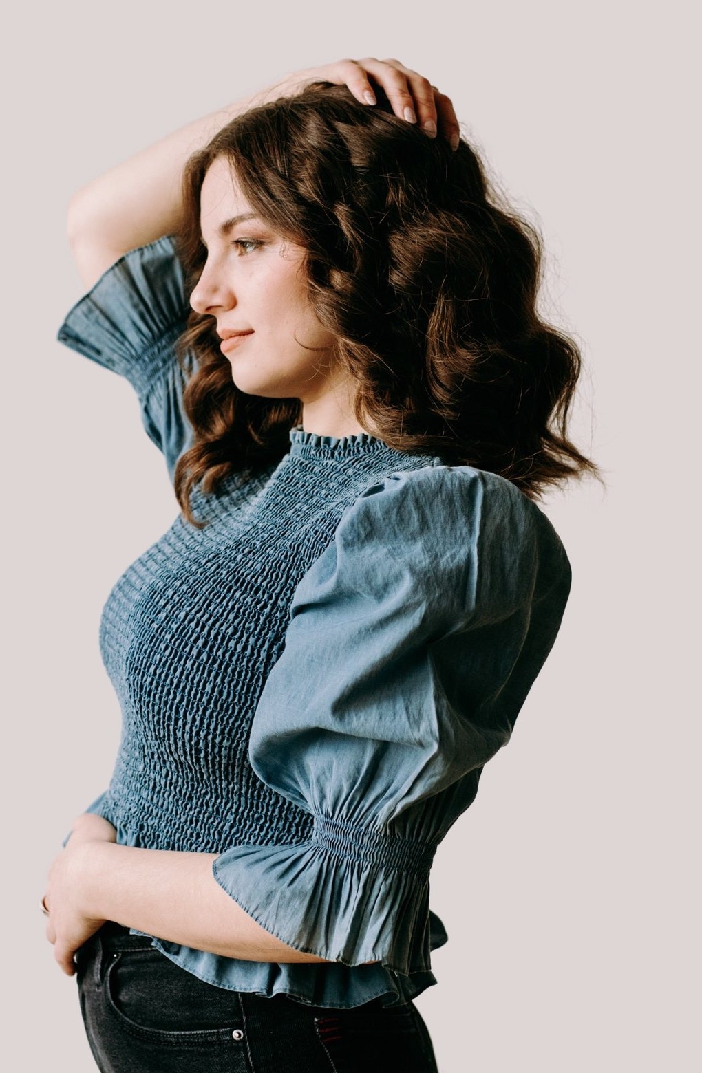 Taryn in profile in a blue smocked top, one hand in her hair
